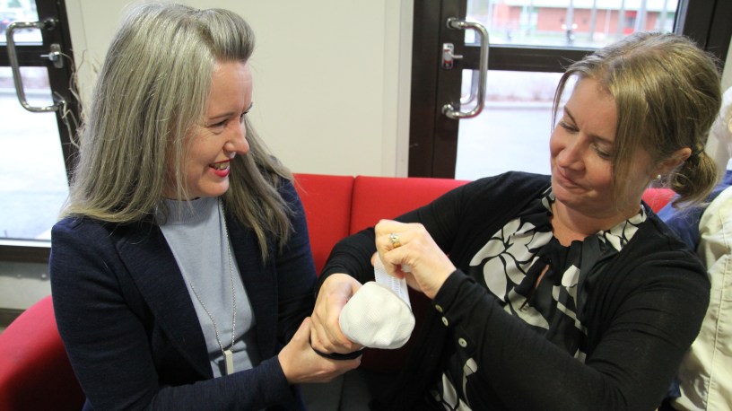 Heli Sulkava ja Titta Vaitiniemi näyttävät, kuinka sidotaan käsi tapaturman sattuessa.